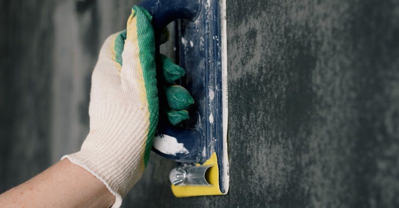 Project Tools - Crop anonymous male worker in gloves holding scraper and aligning walls in flat