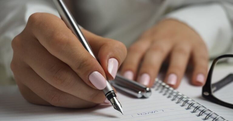 Agenda - Woman in White Long Sleeved Shirt Holding a Pen Writing on a Paper