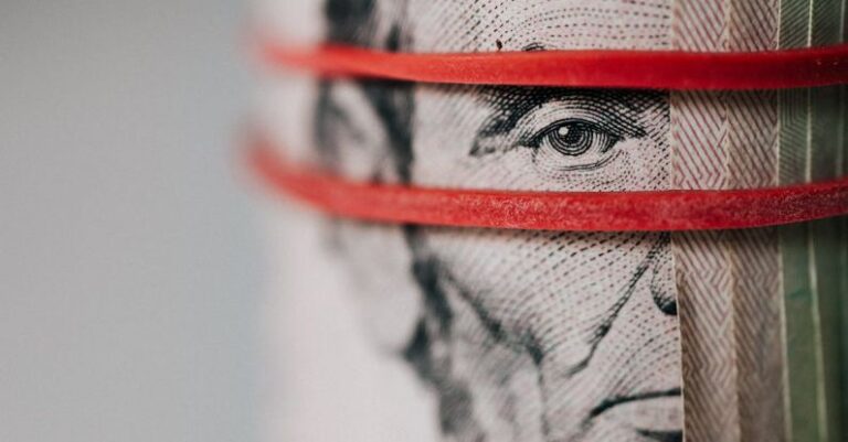 Follow Up - Closeup of rolled United States five dollar bills tightened with red rubber band